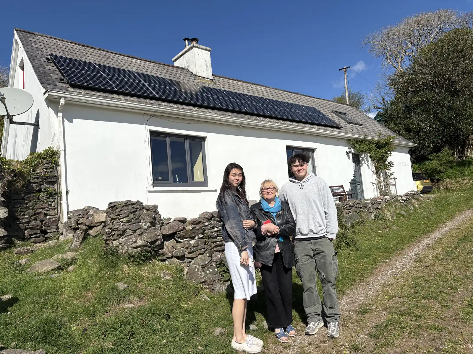 Three people outside the white farmhouse on the family farm in Gleann na nGealt