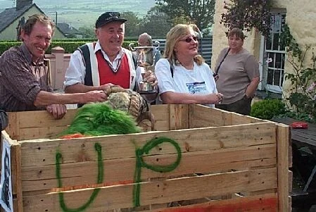 People gathered beside a sheep pen with a trophy at a community fair