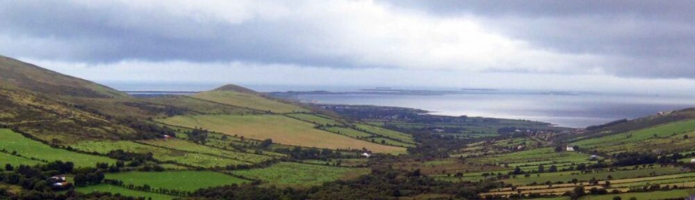 Green fields and hills opening towards the sea in West Kerry